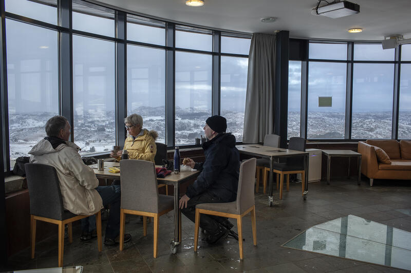 Bilde av tre turgåarar som sit ved bord på kaféen i Kanontårnet med kaffi og kikkar på utsikten.