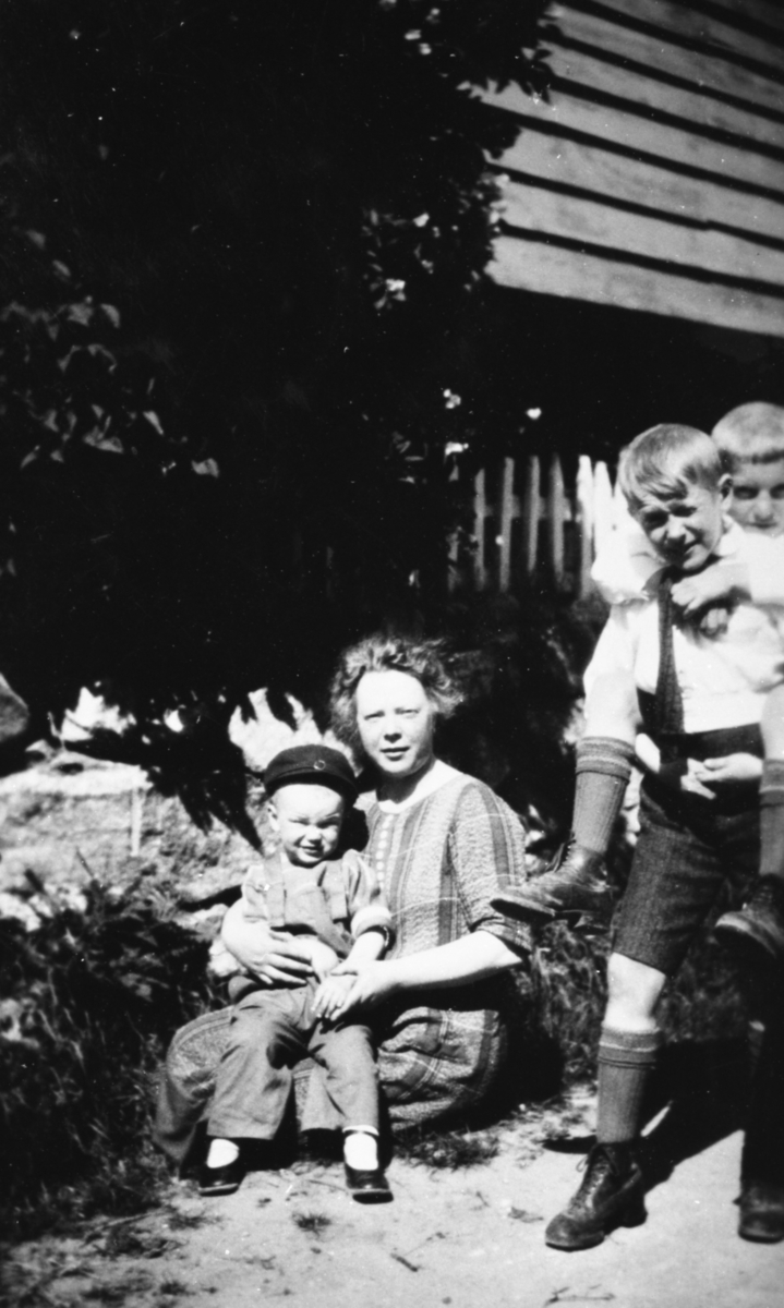 Gruppeportrett av ei ung kvinne og tre barn i hagen foran et hus.
