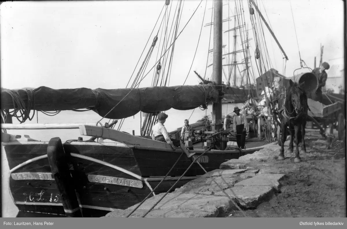 Seilbåten "Prøven" av Svelvik ved Drammen ligger ved brygga i Moss, ca. 1910-20. En mann og to gutter ombord. Lossing av sand. Hest og kjerre.