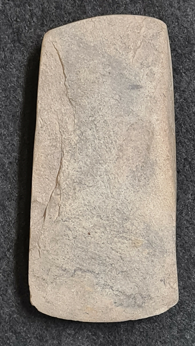 Bergartsyxa tunnackig. L. 9 cm. B. 4 cm. H. 2,1 cm. Yxan är mer eller mindre slipad på alla sidor. Datering 3000-2500 f.Kr.

Ingår i: Arkeologiska fynd från yngre stenåldern funna på/invid Ekholmen i Göta älv, Trollhättan Västergötland fornlämning nr. 205-207. Fynden gjordes vid ett och samma tillfälle av Mika Lädeaho från Trollhättan då han besökte ön i Juni 1994. Föremålen låg spridda som lösfynd i vattnet och längs den eroderade strandkanten på olika platser på ön. Den tunnackiga stenyxan låg öppet på marken ca. 10 meter från stranden.

21 647:1-8
1 Skafthålsyxa, vittrad. L. 14,2 cm. B. 4,7 cm. H. 5,5 cm. Hålets diam. 2,1-1,8 cm. Datering ca. 2000 f. Kr.
2 Bergartsyxa tunnackig. L. 9 cm. B. 4 cm. H. 2,1 cm. Yxan är mer eller mindre slipad på alla sidor. Datering 3000-2500 f.Kr.
3 Trindyxa, vittrad, eggen avslagen. L. 10,6 cm. B. 4,5 cm. H. 3,1 cm. Datering ca. 4000-3000 f.Kr.
4 Knacksten/malsten, förhållandevis jämt rundad. Diam.7-8 cm. Datering: Troligen senneolitikum.
5 Spån och fragment av flinta, 3 st. L. 5,9-3,9 cm.
6 Avslag av flinta, 5 st. L. 4,6-1,5 cm.
7 Flinta övrig, 4 st. varav 1 st. bränd. L. 4,6-2,3 cm.
8 Slagg, svart och porös. 1 stycke delat i två delar. L. 6 cm. B. 2,8 cm. Storleken anger stycket sammanfogat.