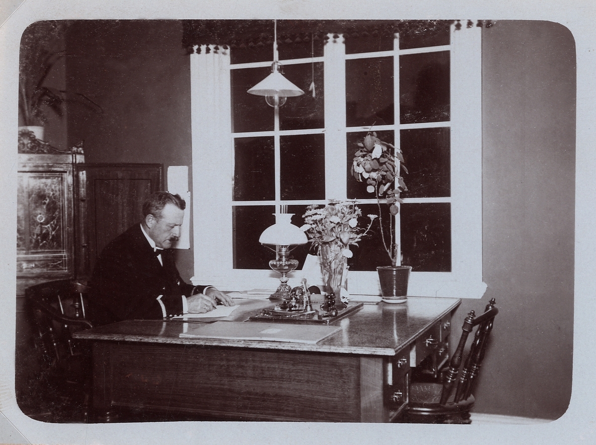 En man i uniform sitter och skriver vid ett dubbelskrivbord, 1910-tal.