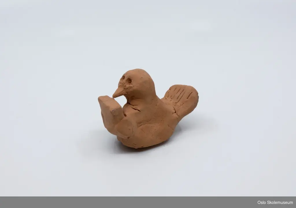 Keramikk figur (fugl). På undersiden av figuren er navnet til eleven risset inn.