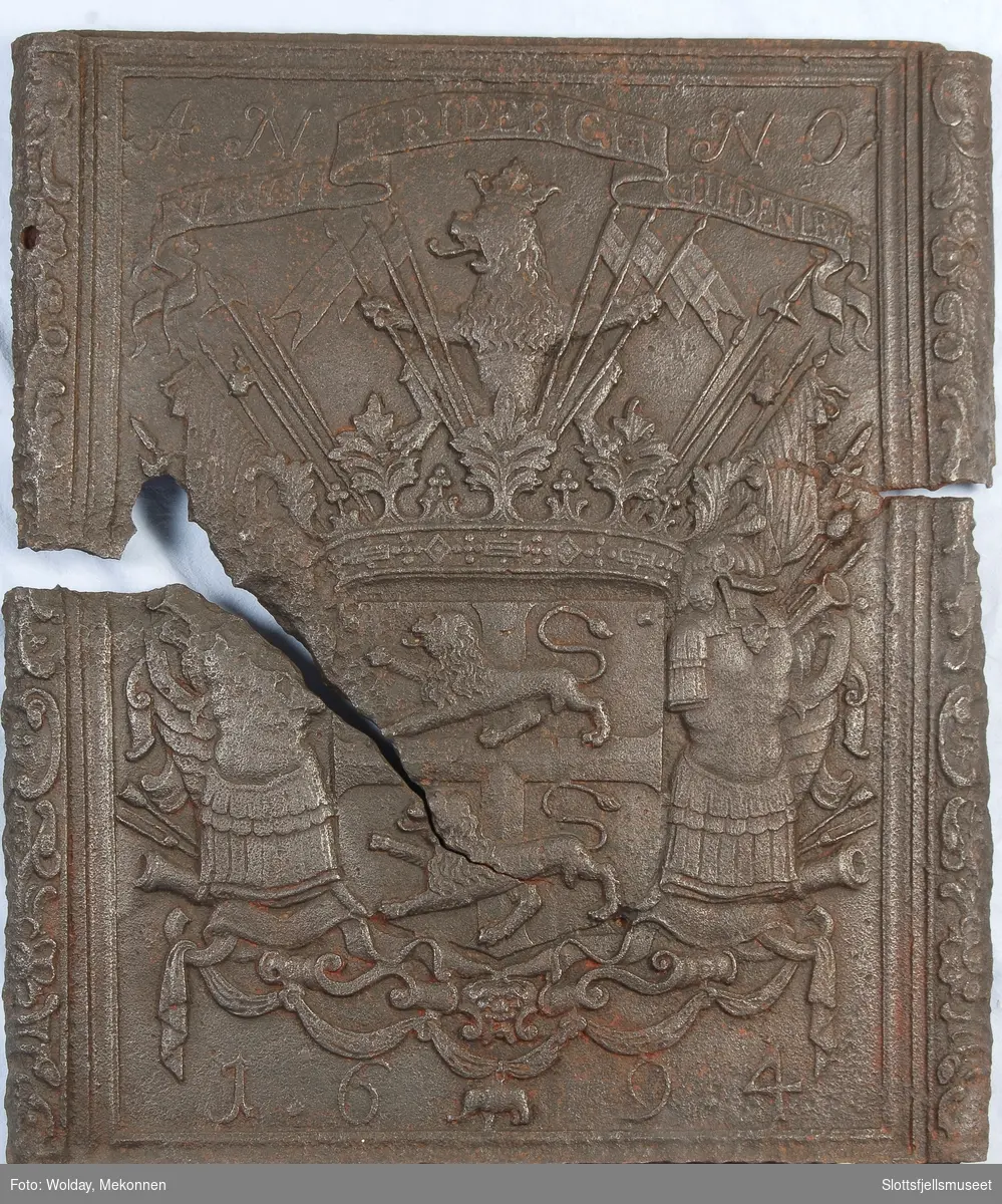 Gyldenløves våpern, omgitt av krigerske emblemer, derover på knekket bånd "ULRICH FRIDERICH"
nederst 1694