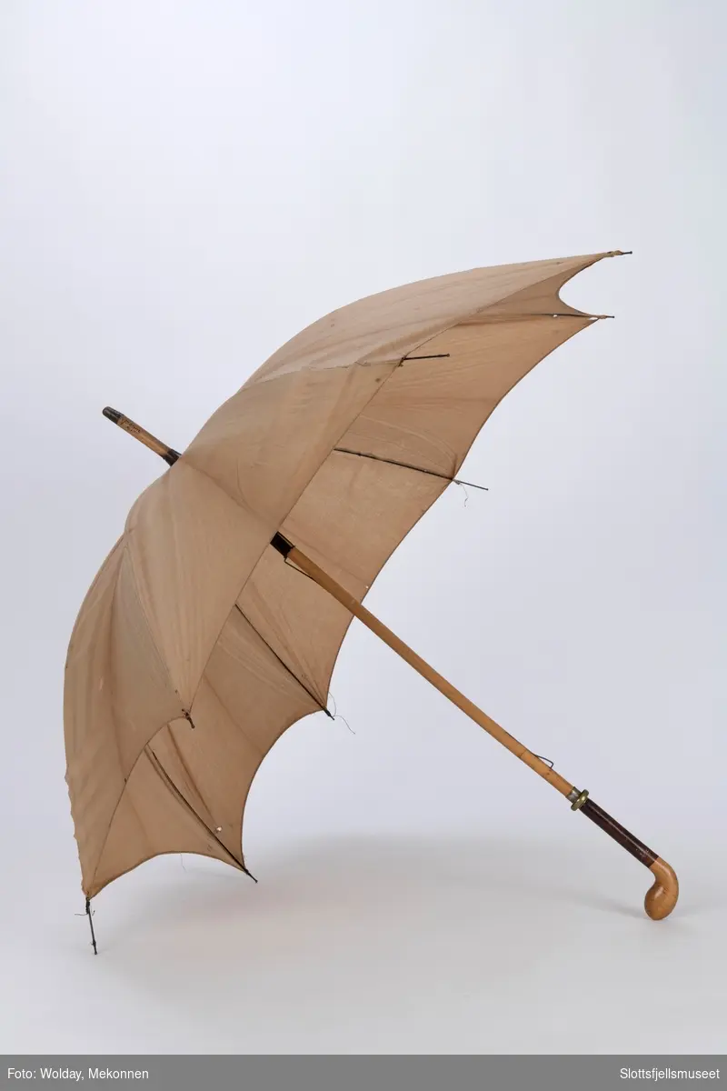 Paraply med 8 spiler i metall og treskaft. Paraply er trukket med lyst bomullsstoff. Treskaftet ender i en kølleformet håndtak. 