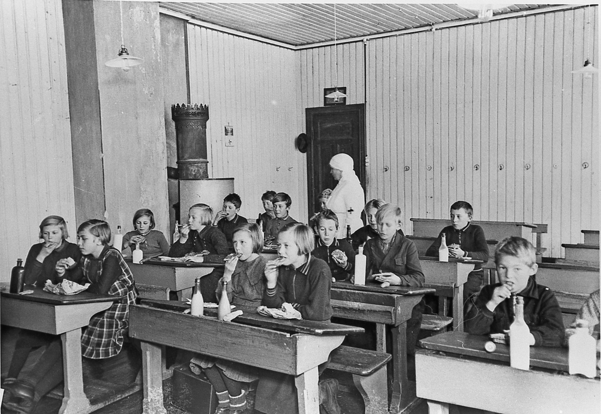 Sigdalsfrokosten demonstreres for lærere og elever ved Kringstad (senere Prestfoss) skole, ca. 1935.  Maten skulle spises først, melkeflaskene står foreløpig urørt. Fremst til høyre: Åsmund Aasly.