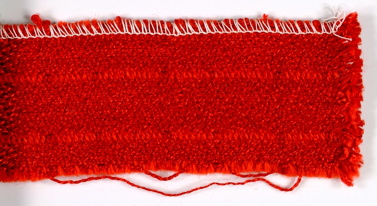 Tygprov vävt i tuskaft med vissa trådar som tvärrips. Varpen är av klarröd rayon. Inslag av rött ylle och röd rayon, samma som i varpen. Rutmönstrat, dels rektangulära (1,8 x 1,1 cm), dels kvadratiska (1,8 x 1,8 cm) rutor. Avgränsningarna utgörs av röd varp och rött inslag. Oliksidigt. En stadkant. Zig-zagad i två kanter med vit tråd.

Tygprov som JM 35460:1 med annan färgställning.