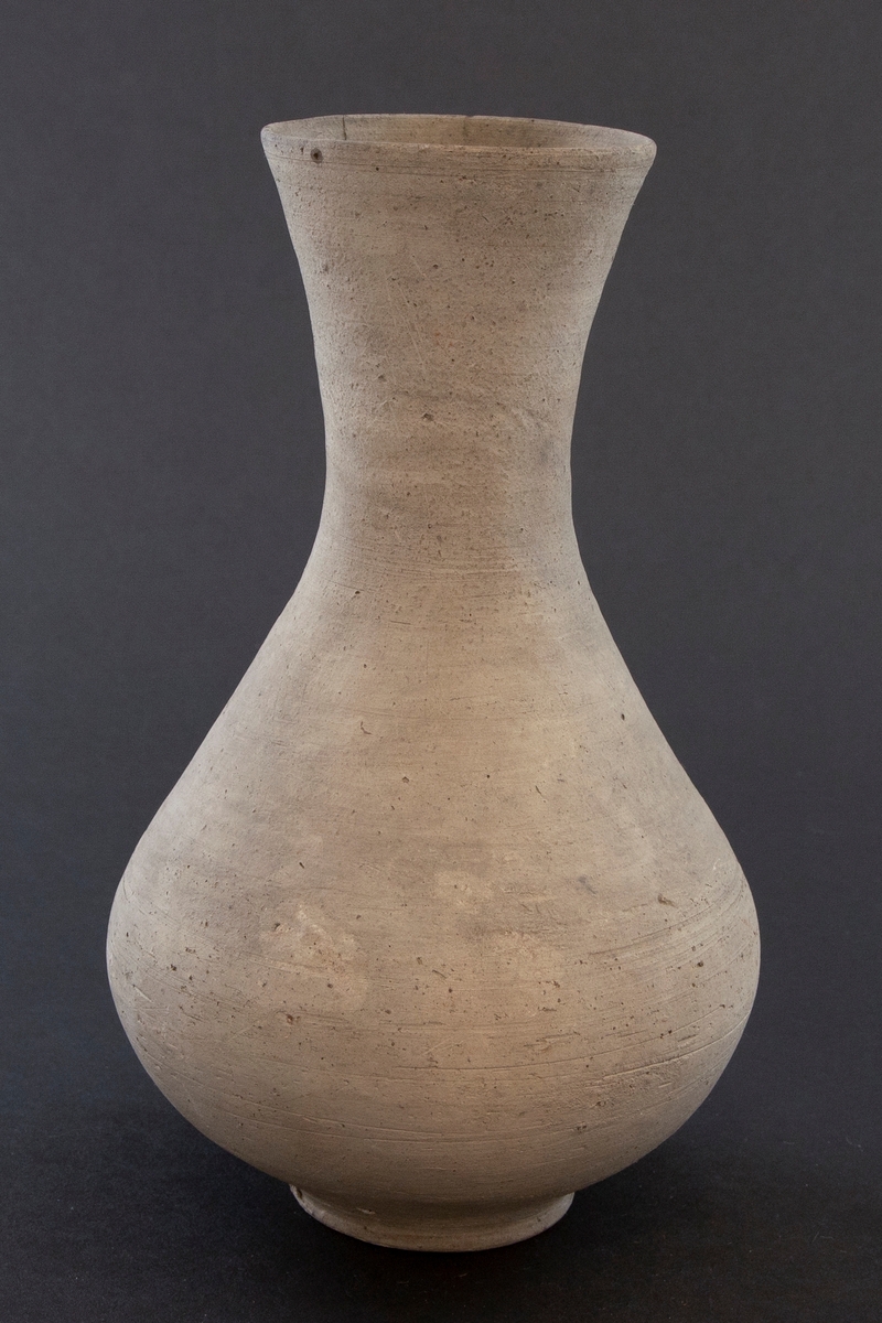 Balusterformet flaske med lav fot og høy hals med utoverbrettet kant. Flasken er dreid i gråbrunt leirgods og er uglasert.
