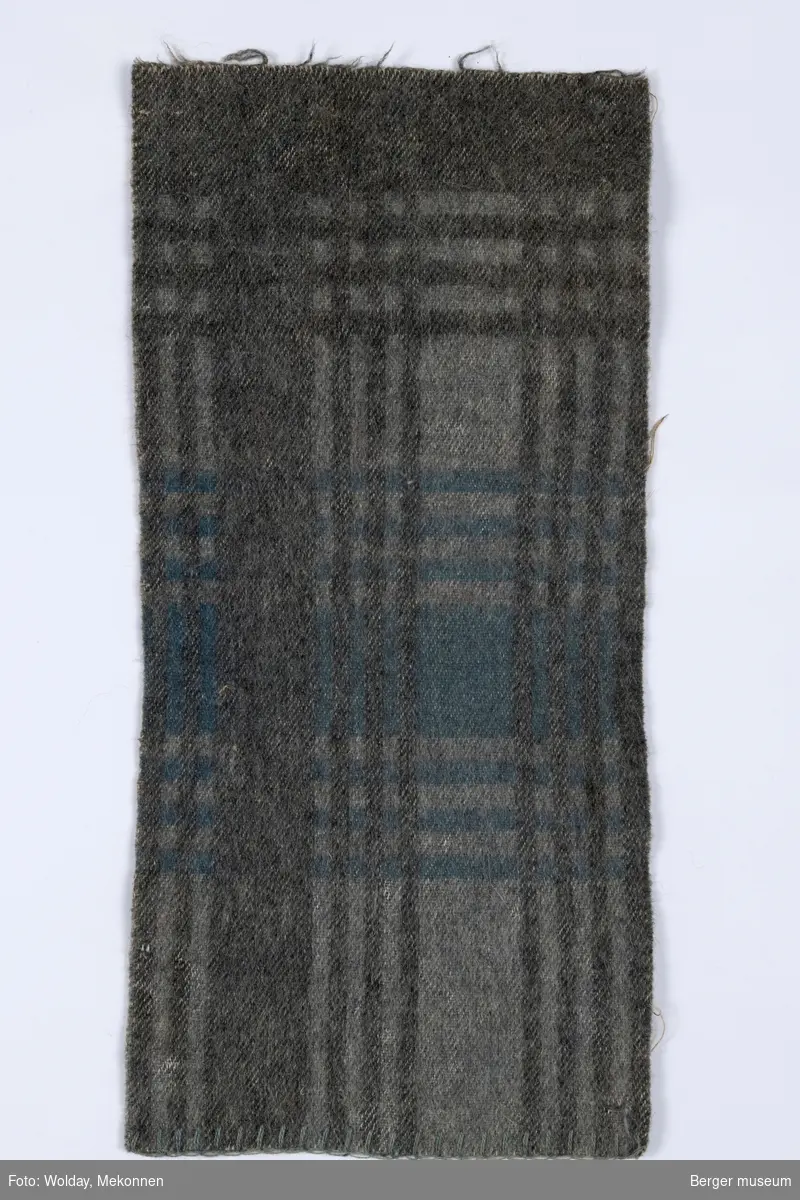 En prøve. Teppe med rutete mønster som er skapt av brede og tynne streker på tvers og på langs på teppet.