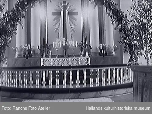 Interiörbild av koret i Fagereds kyrka i Halland. Altare, altarring och altartavla samt främre hörnet av ett bänkkvarter som är ådringsmålat. Koret är lövat med såväl en båge som en späd björk.