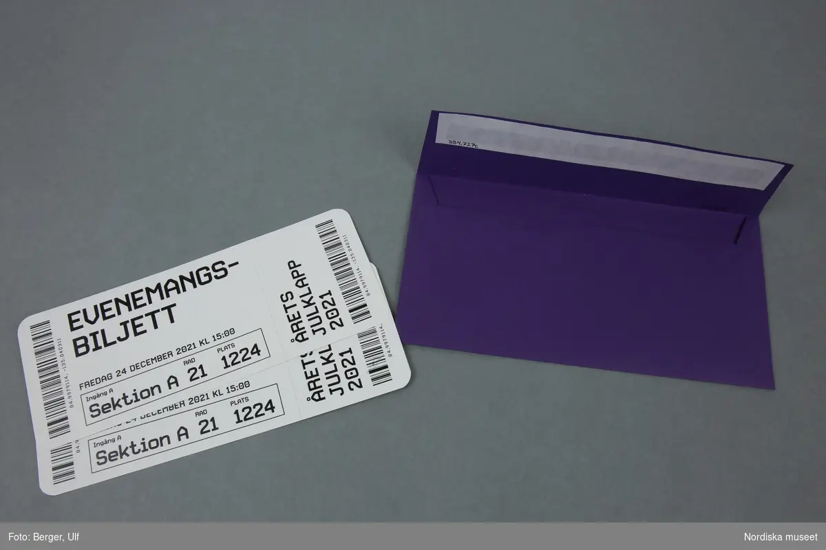 a-b) Två stycken vita pappersbiljetter med svart trycktext i ett c) lila kuvert.