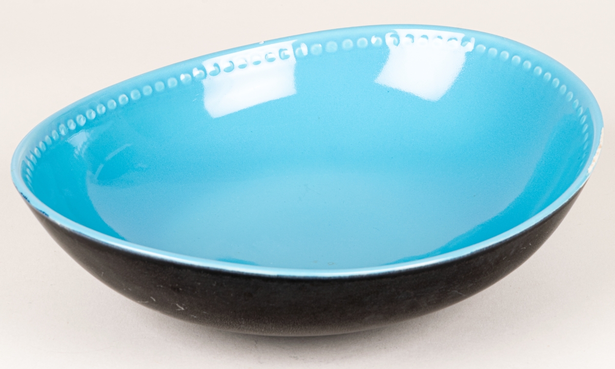 Större oval skål i flintgods med dekor Indiana i modell LE2, forrmgiven av Arthur Percy för Gefle porslin 1957. Insidan har turkos glasyr, utsidan har den matta svarta glasyren Negro. Längs skålens kant på insidan finns upphöjda dekorativa prickar i godset.