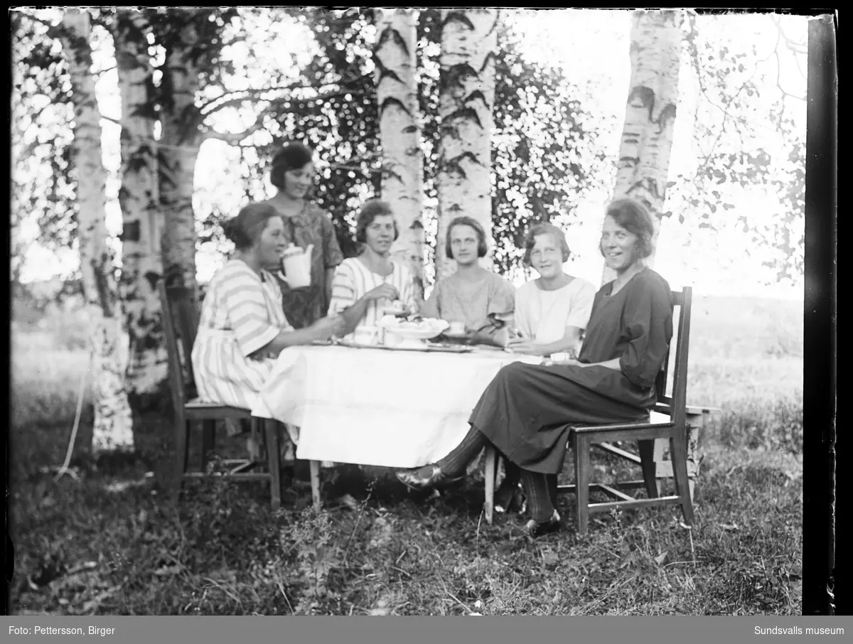 Sex unga kvinnor ligger i gräset på gården Ystibacken i Mjösund, Njurunda. På bild två sitter de och fikar i trädgården.
