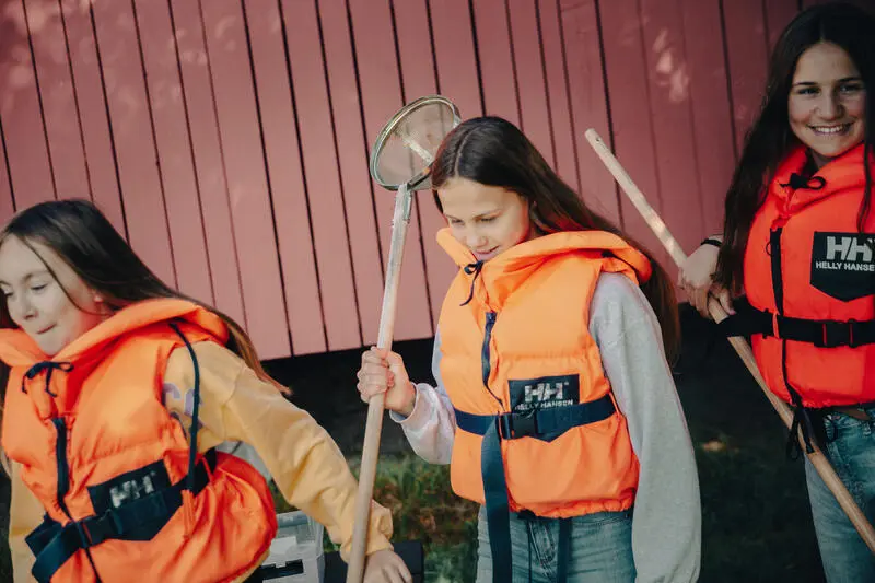 Foto av tre jenter som har på seg redningsvest og har utstyr klart til å fange insekter i vann