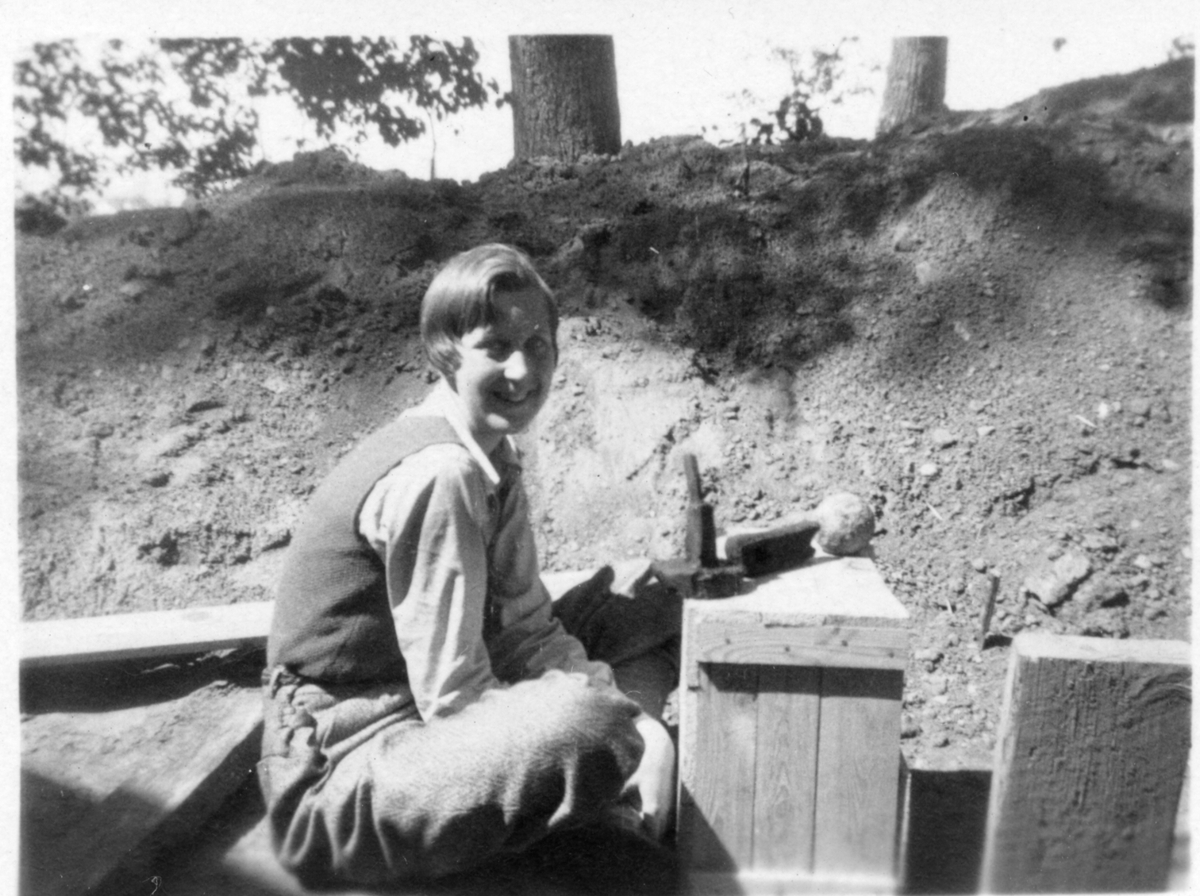 Fröken Ingegerd Sjöberg från Stockholm sitter vid en låda med fynd från den arkeologiska utgrävningen vid Rumlaborg i Huskvarna sommaren 1932.