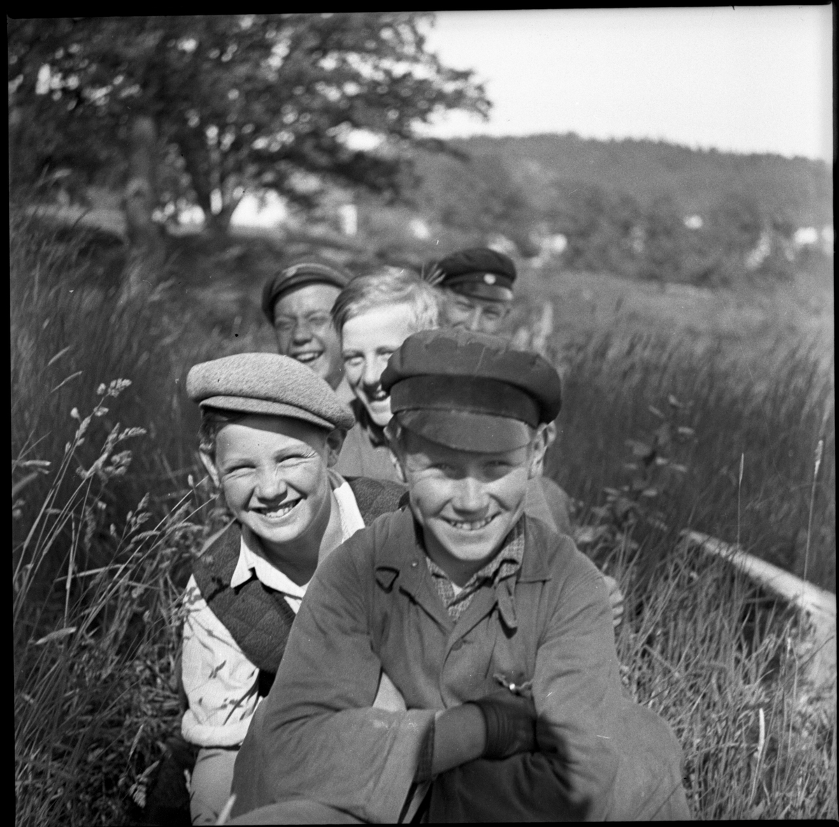 Fem glada pojkar sittandes i gräset vid Rumlaborg i Huskvarna sommaren 1935. Pojkarna hjälpte till vid en arkeologisk undersökning som bedrevs av Huskvarna hembygdsförening.
