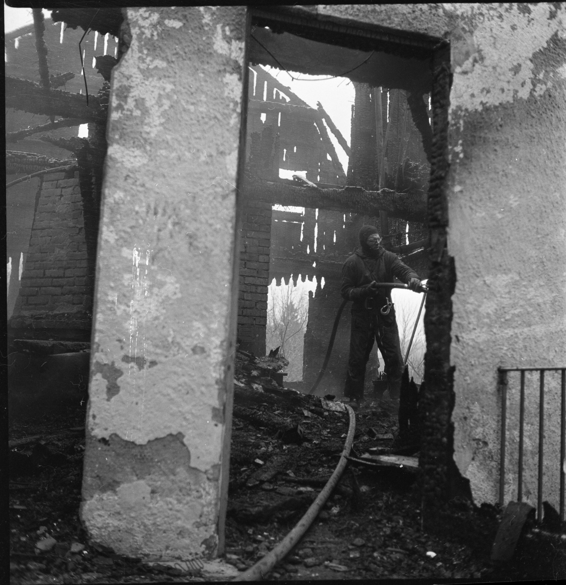 En brandman med slang står inne i ett kraftigt brandskadat putsat hus.