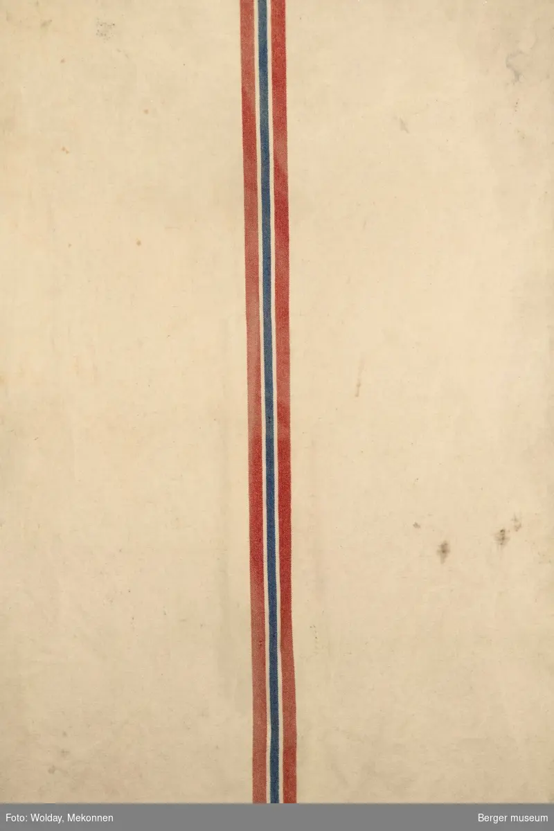 Et hvitt møkkete teppe, også kalt hesteteppe, med rød, blå og rød stripe i midten, som minner litt om det norske flagget.