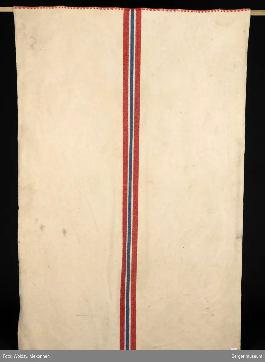 Et hvitt møkkete teppe, også kalt hesteteppe, med rød, blå og rød stripe i midten, som minner litt om det norske flagget.