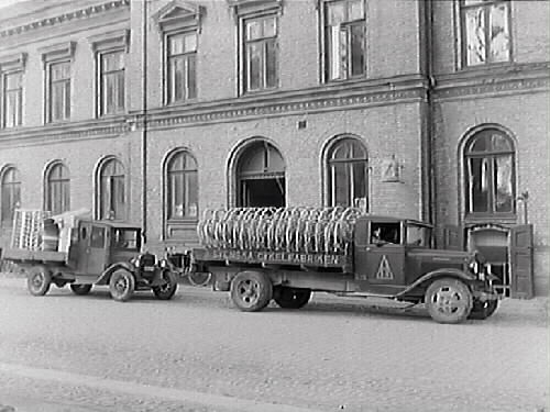 En större lastbil, "Svenska Cykelfabriken" med cykelhjul på flaket, samt en mindre vid Rommelska fastigheten i Varberg. (Svenska Cykeldepoten bytte 1925 namn till Svenska Cykelfabriken, som i sin tur ändrades till Svenska Cykelfabriken Monark år 1934)