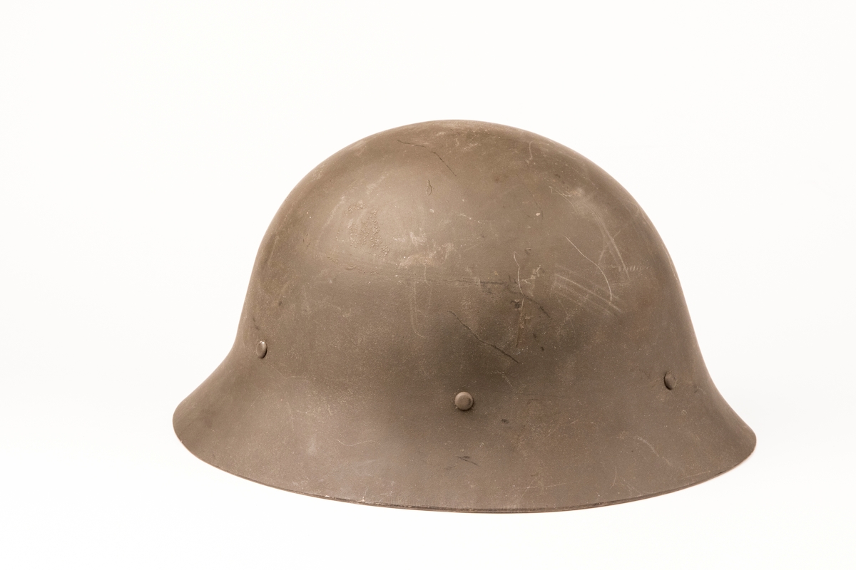 Hjälm för civilförsvar (m/1926) av stål med utåtböjt brätte och hakrem av läder och metallspänne. Inredningen är av läder med tre tygkuddar. Oanvänd.