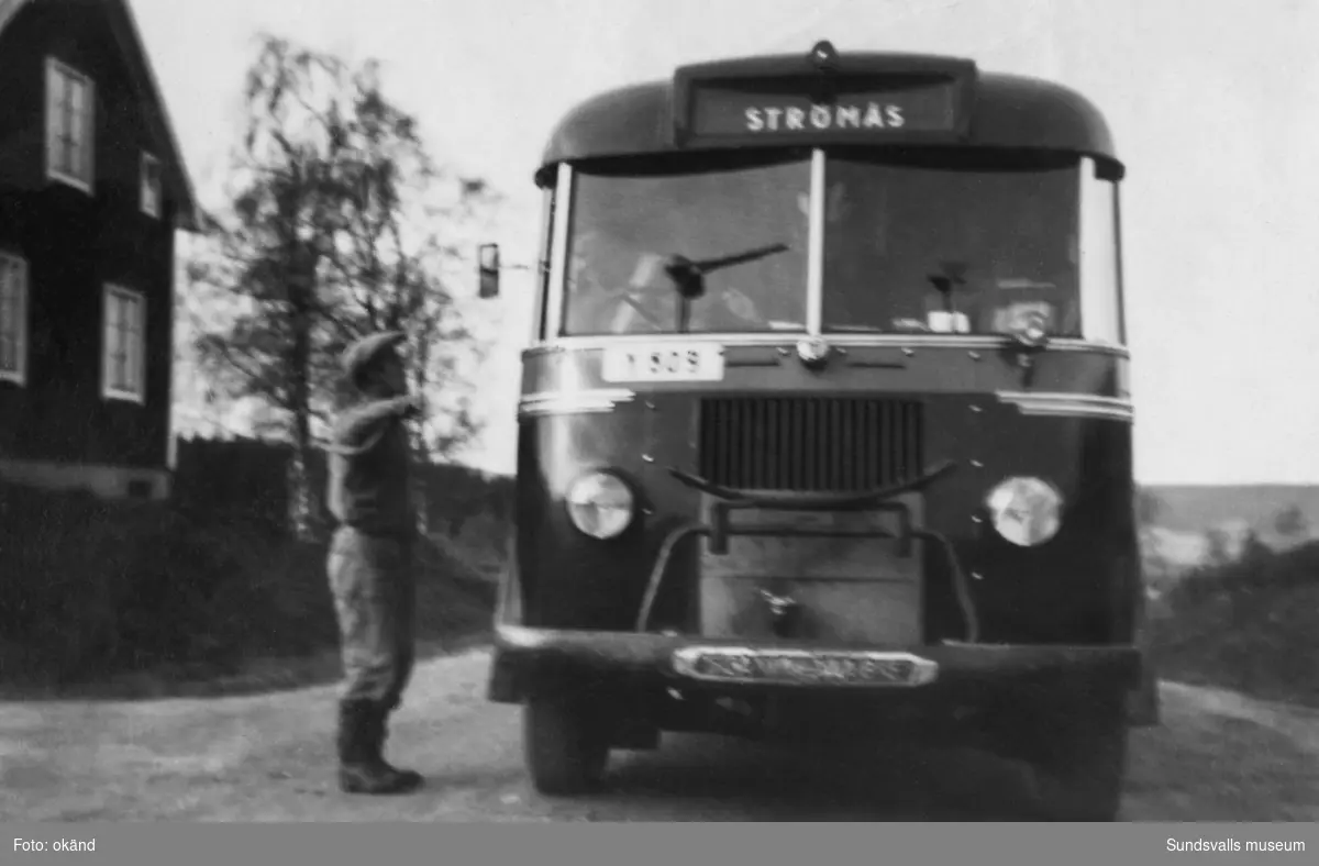 Bussen till Strömås, Sättna, står på landsvägen mellan Timrå och Kovland, alldeles vid infarten till Brödlösa, och en man samtalar med chauffören. Huset i bildens vänsterkant finns ännu (2023) kvar. Ur en samling som tillhört Rodin/Öhlén, Kovland.