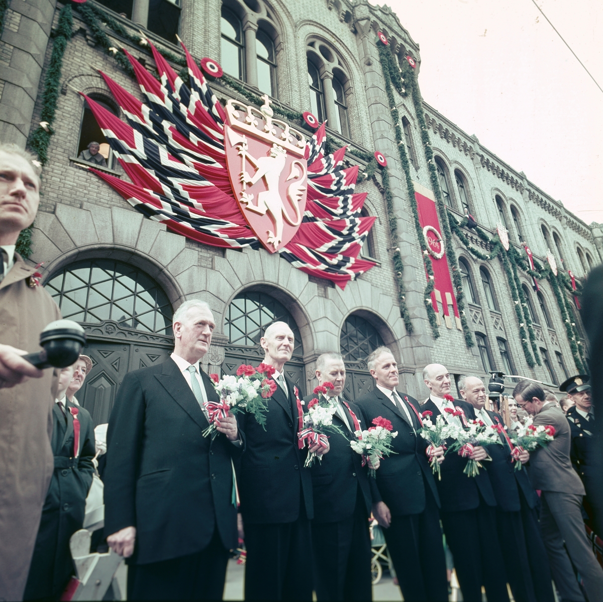 Stortingets presidentskap står foran et pyntet Storting i forbindelse med Grunnlovsjubileet i 1964.
