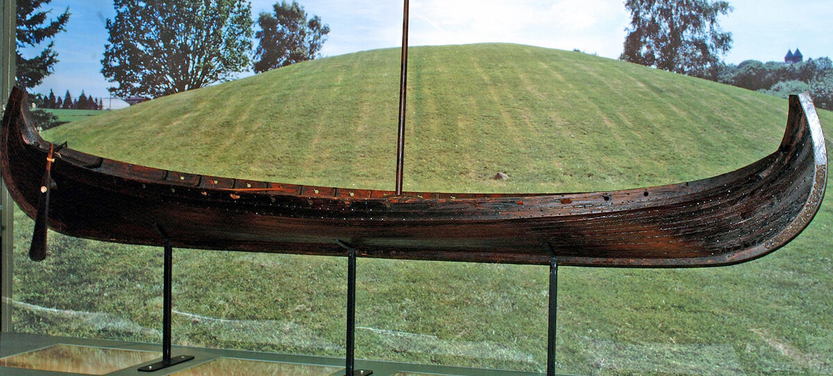Bildet viser en kopi av Osebergskipet foran gravhaugen.