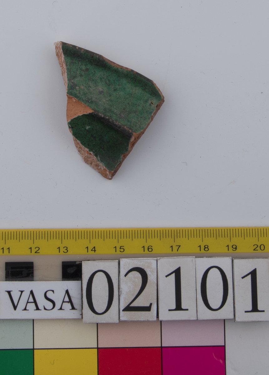 Två skärvor från ett grönglaserat keramikfat.
Fragment av mynningsrand (bräm) med bit av plan botten av fat. Profilerad bräm. Insida blyglaserad grön. Utsida oglaserad. Undersidan av den platta botten är räfflad.
