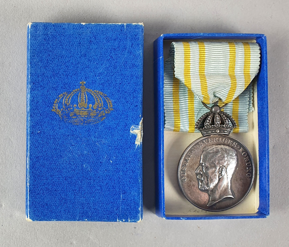 Sølvfarget minnemedalje med motiv av Kong Gustaf V i profil på den ene siden og tre kroner på den andre siden. Det er festet et opphengsbånd til medaljen. Med medaljen følger det en blå eske..
