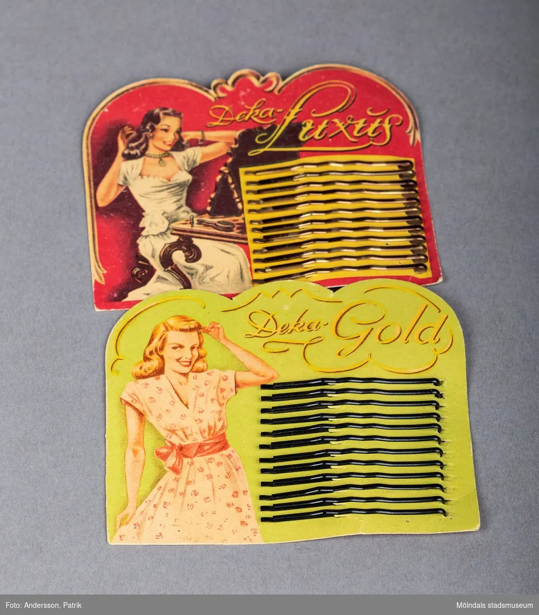Två kuvert med hårnålar från 40- 50-talet. Det ena kuvertert är rött till färgen med en sirlig guldkant. Det står Deka Luxus på framsidan och till vänster finns en bild med en vacker kvinna i vit klänning som sitter och tittar sig i en spegel och gör i ordning sitt hår. Det andra kuvertet är grönt. Även detta kuvert har en sirlig guldinramning. Till vänster på denna förpackning finns en liknande bild med en ljushårig kvinna iförd en blommig sommarklänning. Kvinnan ler och håller upp en hand i håret.