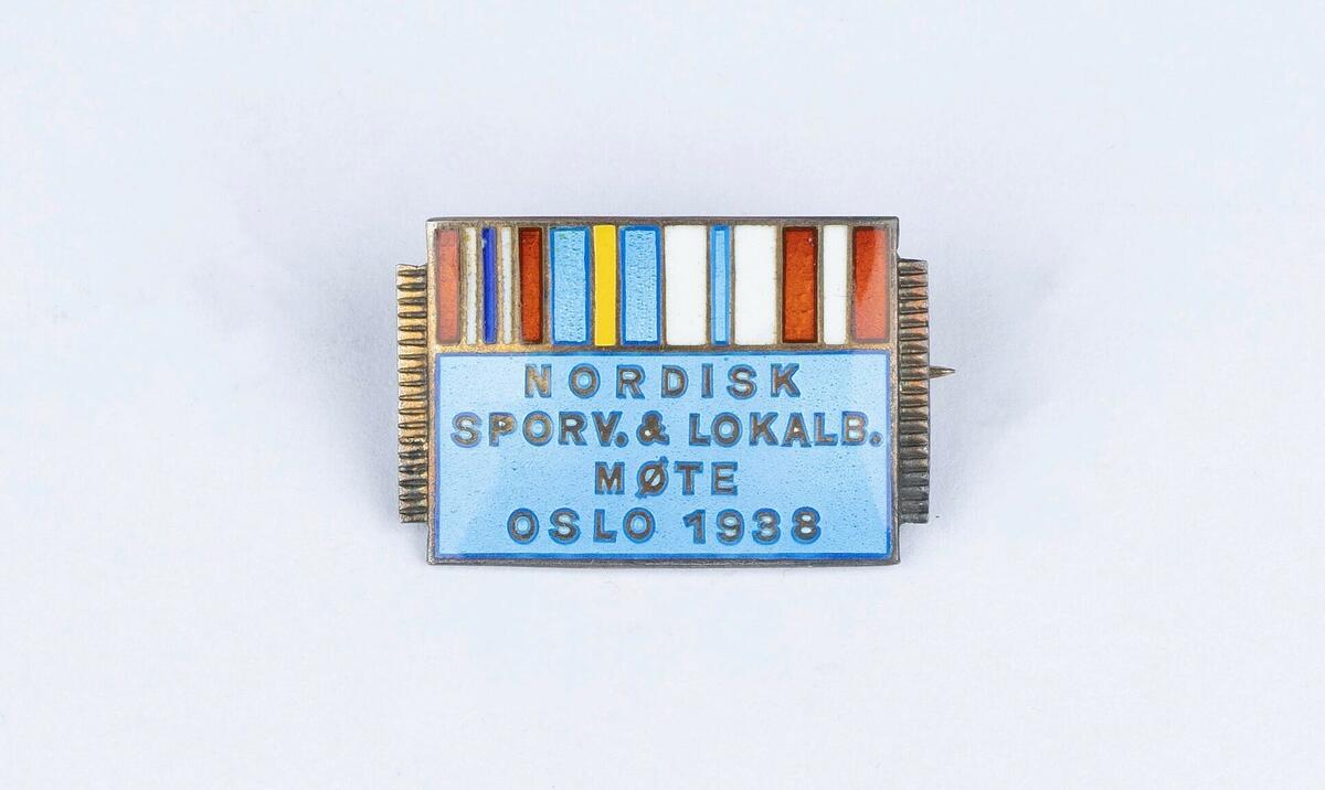 Jakkenål i lys blå farge med striper i rødt, hvitt, blått og gult over og med skriften "Nordisk sporv. & lokalb. møte Oslo 1938".