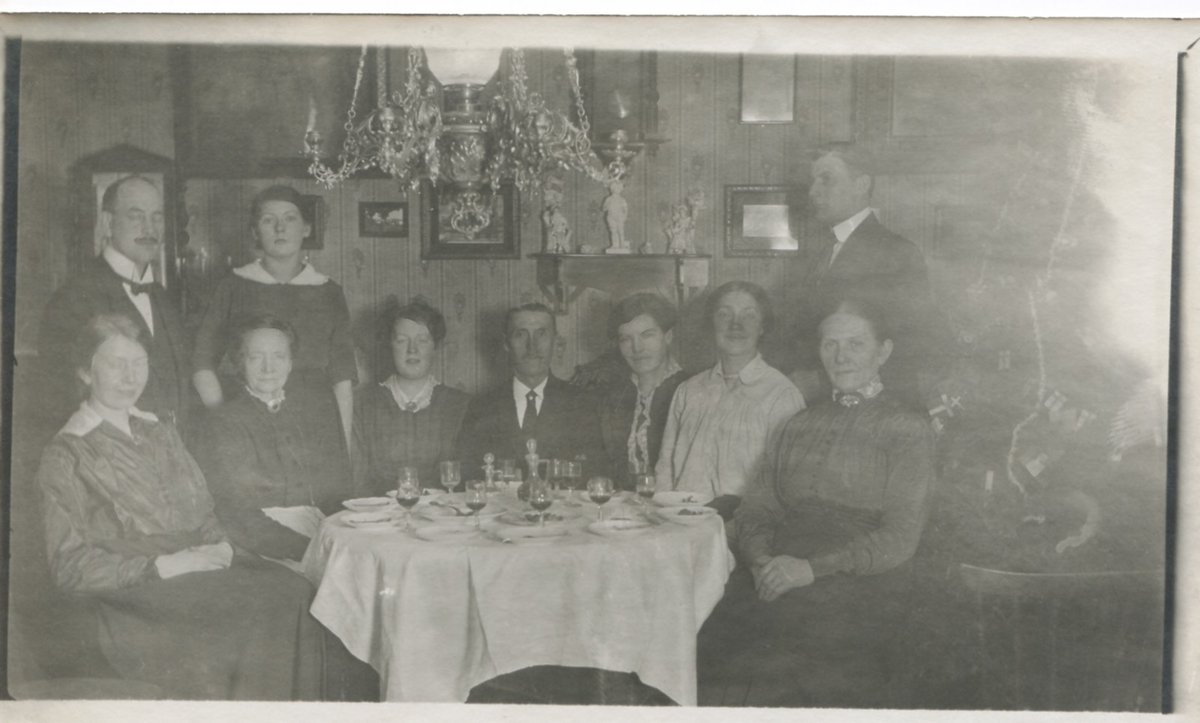 Bjudning i ett välbärgat hem där personer sitter samlade runt ett bord, okänd plats 1910-1920. Femte person från vänster: Hilda Sandberg (1887-1973, född Olsson).