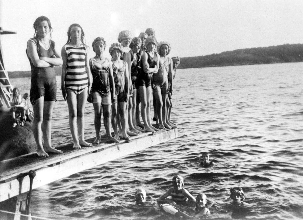 Svart hvitt bilde av barn på stupebrett over sjøen, med flere barn uti vannet (Foto/Photo)