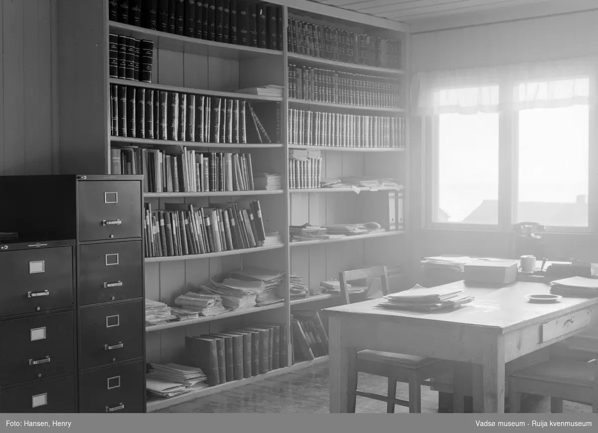 Kontorinteriør med bokhyller, arkivskap og skrivebord, trolig på et statlig kontor i Vadsø i 1957.
