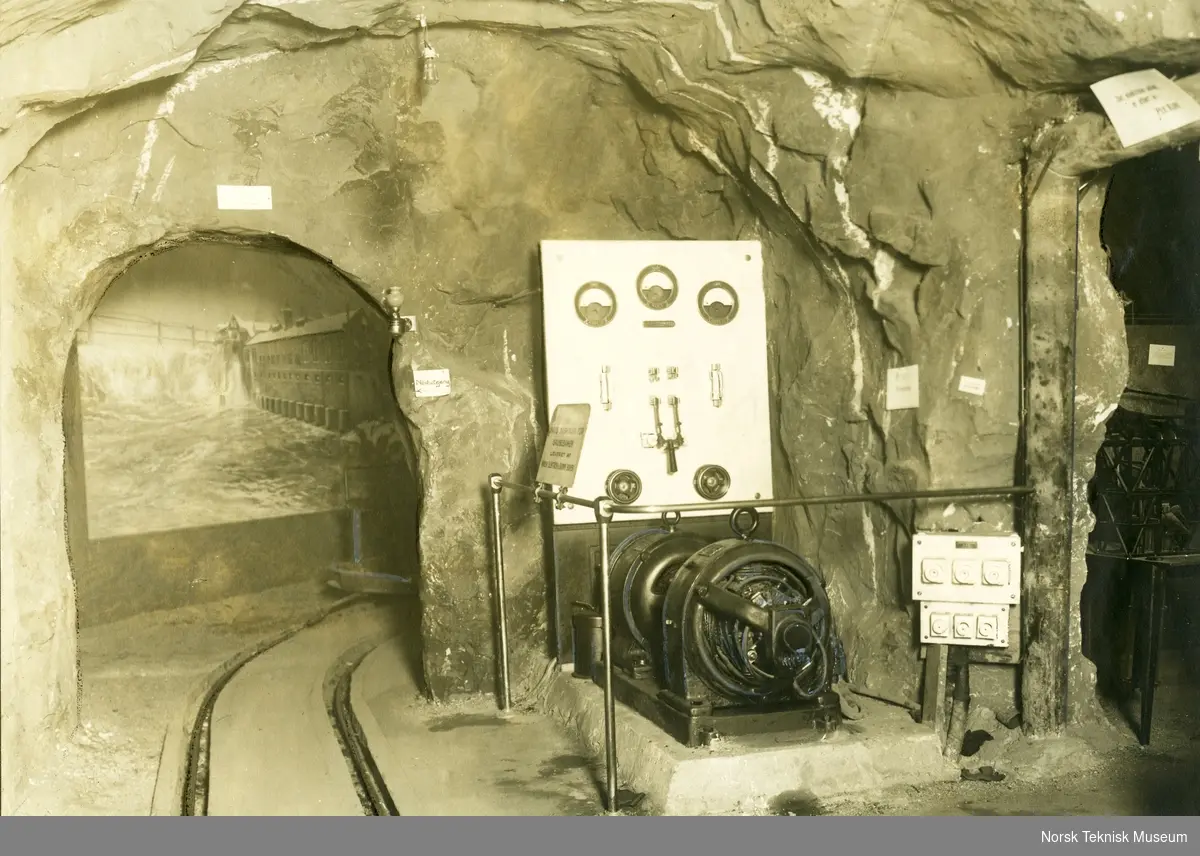 Omformerstasjon for grubelokomotiver, fabrikat Norsk Elektrisk Brown Boveri. Bildet er fra jubileumsutstillingen på Frogner i 1914 og viser en omformerstasjon med apparattavler plassert inne i en tunnell