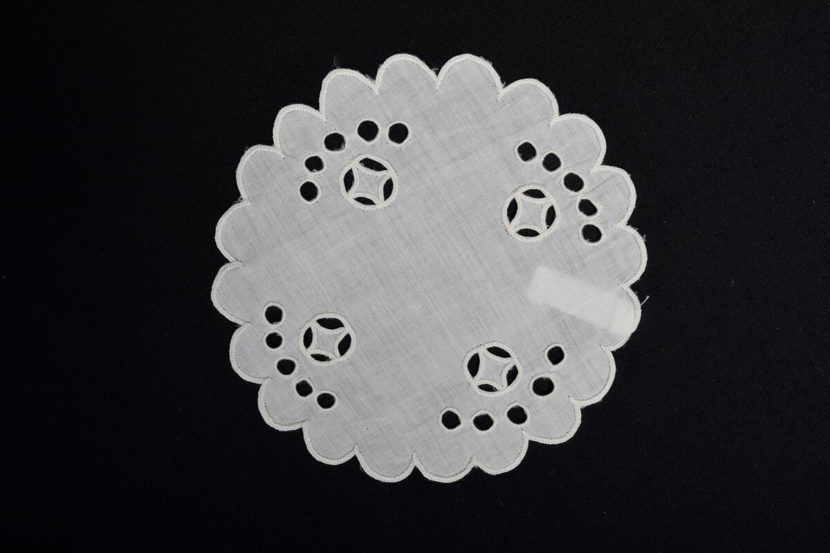 Tablett av vitt tuskaftat bomullsväv med utklippssöm, så kallade engelska hål broderade med vitt bomullsgarn. Tabletten är tillverkade av givarens mor Elise Hofmann (1891-08-23 – 1964-03). 