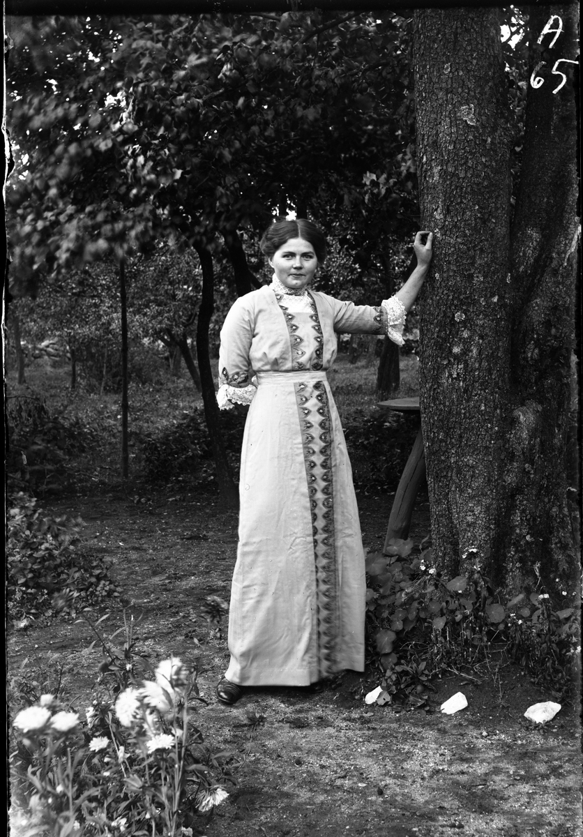 Jenny Eklöw på Mossagården i Torpa står i trädgården med handen mot ett träd. Runt trädet växer krasse och vitmålade stenar ligger som dekoration längs gången. (Se även bild nr GEA003)