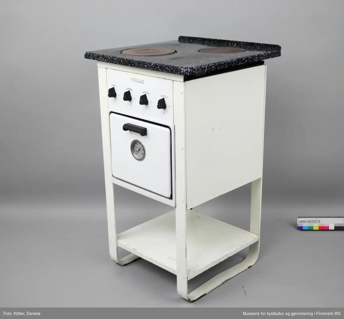 Den elektriske komfyren "Vegar K2" har to kokeplater, en stekeovn og en hylleplate nederst. Fram- og bakben er utformet som buer på hver side. Apparatet har fire vrideknapper, en for hver plate, samt for over- og undervarme i ovnen. På ovnsdøra er det et rundt termometer som viser temperaturen i ovnen. I ovnen er det to lave og et dypt stekebrett, samt en rist. Typeskiltet befinner seg på baksida. Strømkabelen er svært porøs og mye av isoleringen har falt av.