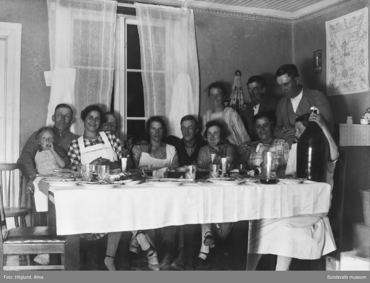 Ett uppsluppet sällskap samlat vid matbordet, elva vuxna och ett barn. Stående längst bak Alma och, längst till höger, Gottfrid Höglund. Övriga är oidentifierade.