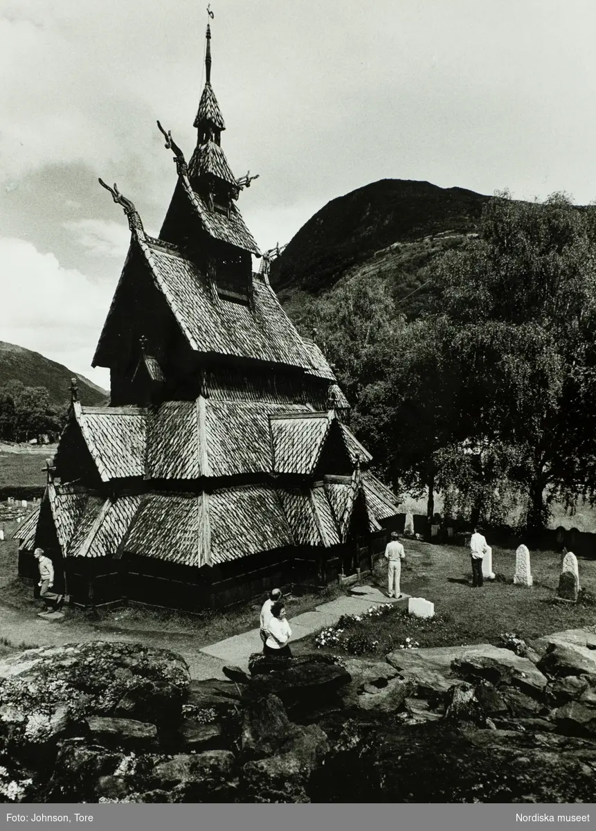 Borgunds stavkyrka i trä, Sogn og Fjordane fylke i Norge. Kyrkan från 1150, är en av de mest typiska och bevarade stavkyrkorna i landet. Några människor syns utanför på kyrkogården.