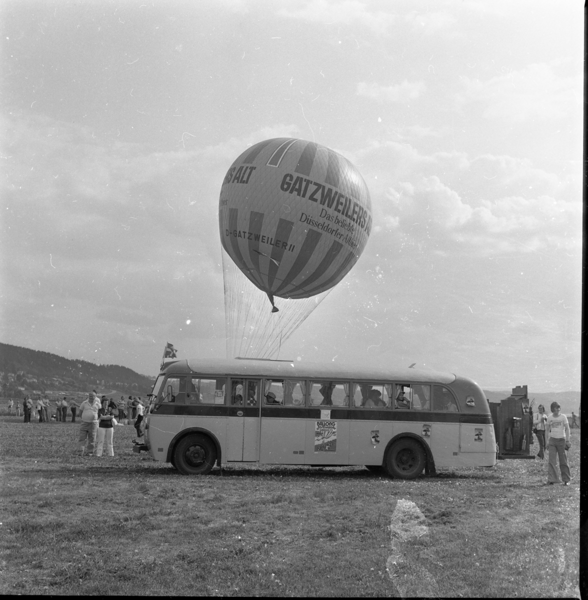 En västtysk gasballong märkt Gatzweilers Alt står beredd att lyfta. Hitom den står en veteranbuss. På sidan sitter en affisch för Ballongfestivalen i Gränna. Bussen tillhör Knut Johansson.