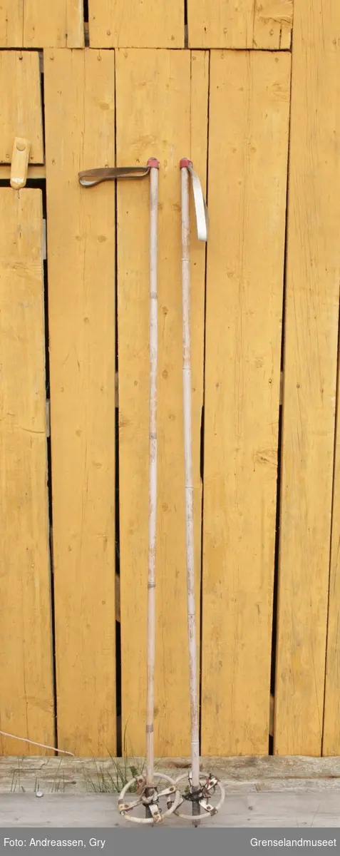 Et par skistaver av bambus, med hvite stropper av skinn- en rød skinnstrimle er festet rundt staven og stroppen for å holde den på plass. Trinser av bambus og hvitt skinn. Tupp av messing og spiss av jern.