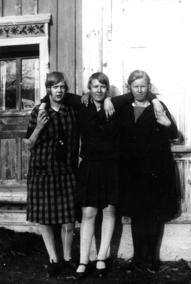 Tre unge kvinner poserar framfor ein husvegg.