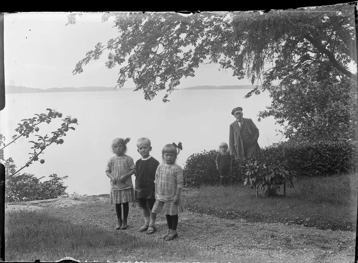 Barn och man i trädgård vid vattnet, Krusenberg, Uppland