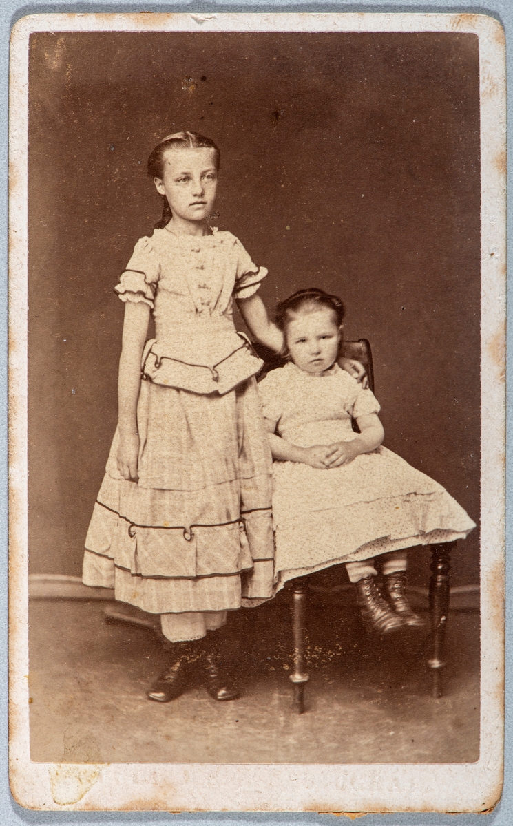 To jenter, Ragnhild Holte (f: 1863) 12 år og Anne Holte (f: 1872) 3 år, sittende i stolen.  Carte visit og Kabinett bilder fra to fotoalbumer fra Holte Gård i Stange.