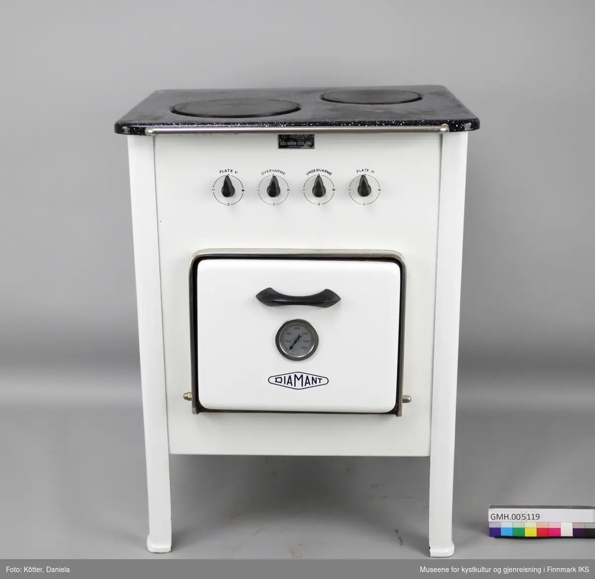 Den elektriske komfyren "Diamant PK 2" har to kokeplater og en stekeovn. Apparatet står på fire ben og har fire vrideknapper, en for hver plate, samt for over- og undervarme i ovnen. På ovnsdøra er det en rund termometer som viser temperaturen i ovnen. I ovnen er det to lave og et dypt stekebrett. Foran på toppen er det en sølvfarget stang.