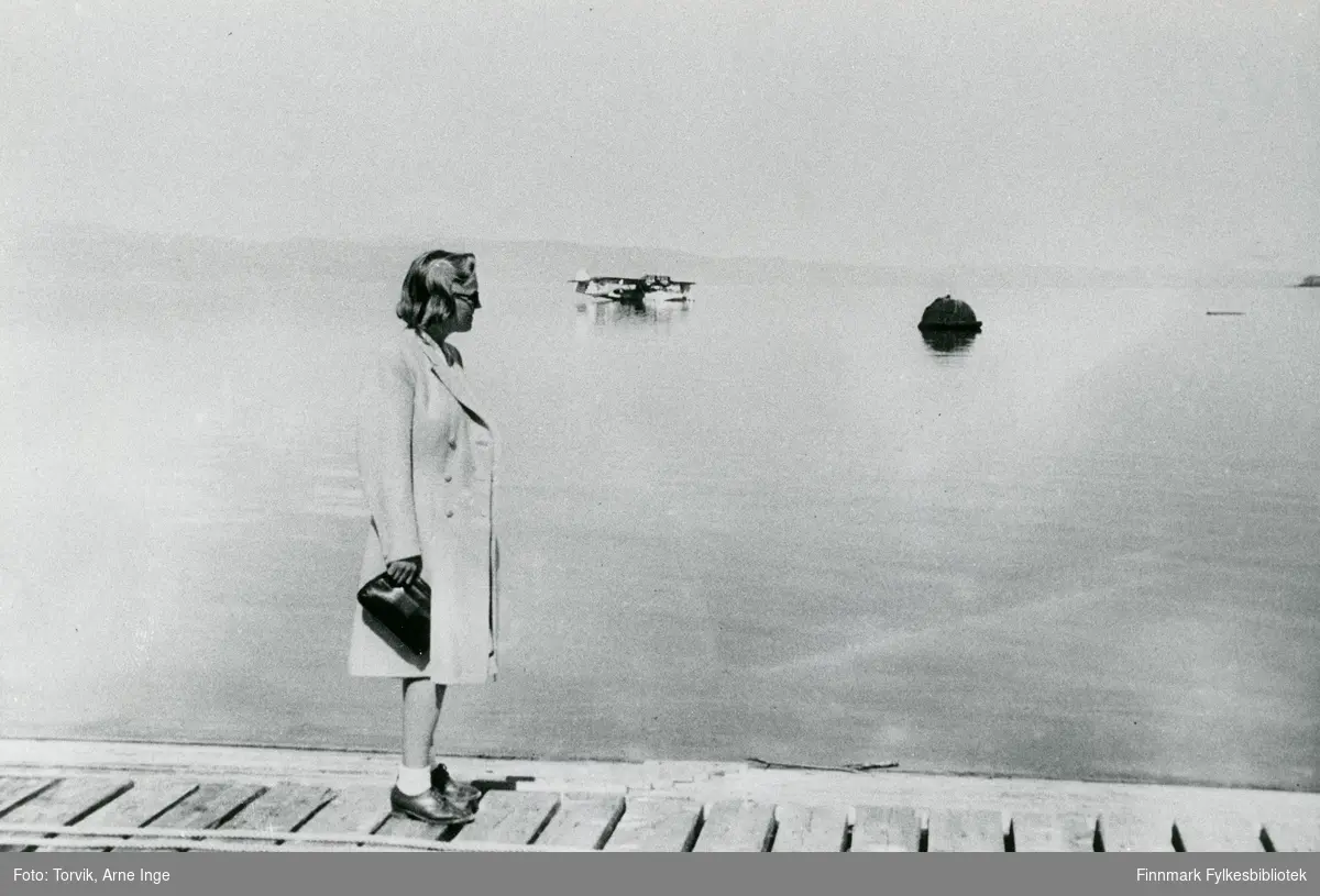 En ukjent dame står på dampskipskaia i Vadsø havn i 1947. I bakgrunnen ser vi et sjøfly. På den tiden var det havnebassenget som var flyplassen i Vadsø.