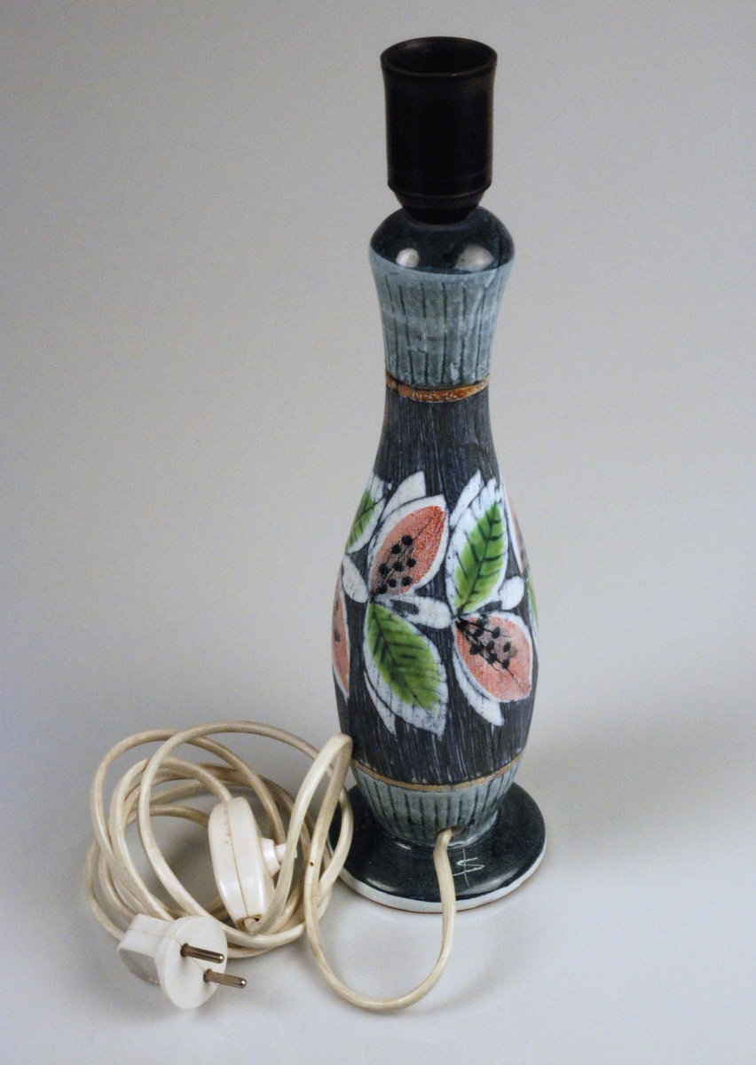 Lampfot i blå sgraffito-teknik och blomdekor i grönt och rosa. Glaserad. 

Tillverkare är Tilgmans Keramik i Göteborg, ett företag som var en viktig inspirationskälla för Alingsås Keramik under 1950-talet. 

Stämplar under: 
Tilgmans Keramik
Made in Sweden