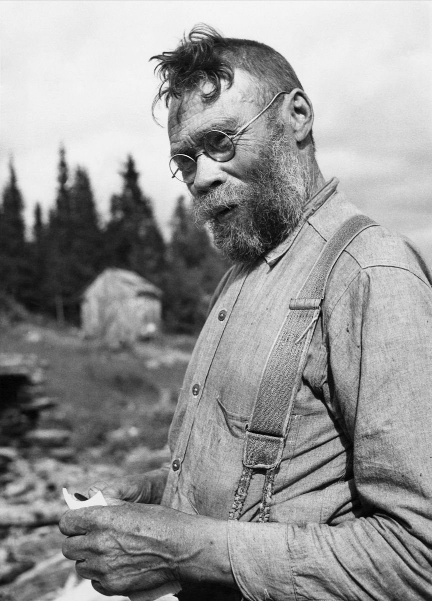 Porträtt av båtbyggaren Jonas- Paul i Lövbergs by. Man med skägg, glasögon, arbetsskjorta och hängslen.