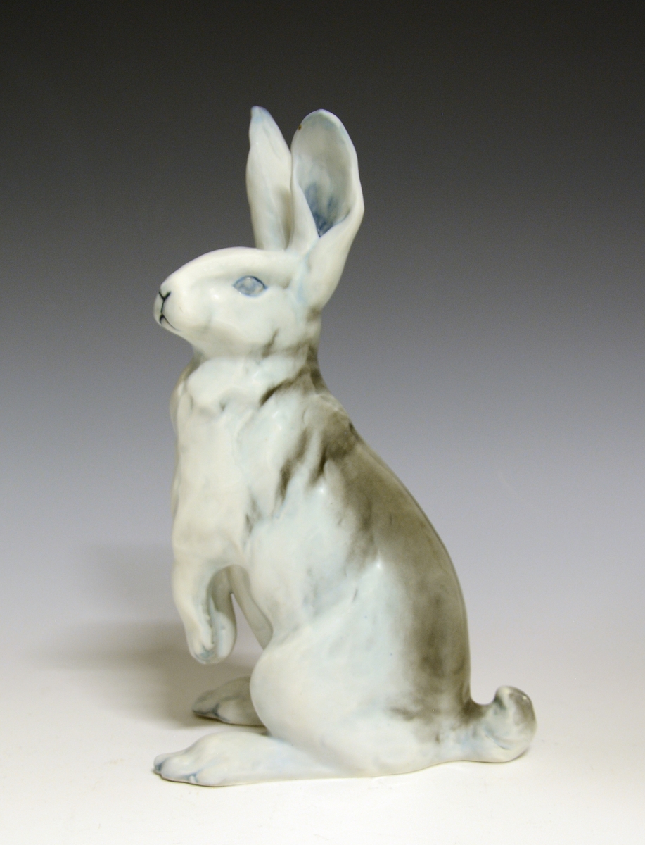 Prot: Figur av porselen. Hare sittende på bakbena. Blågrå farger, glasert (underlagsfarge). Design: Sirnes, prod. 1910.
Modellnr: 1952